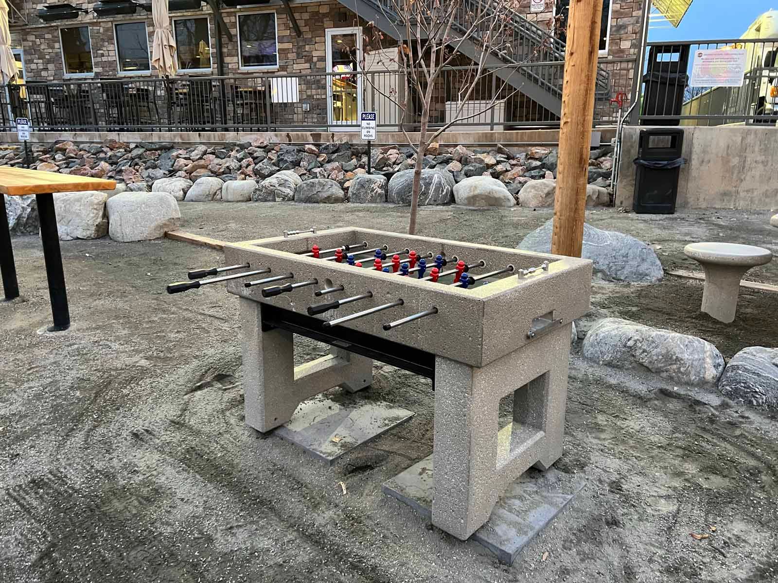 A foosball table is sitting in the dirt in front of a building.