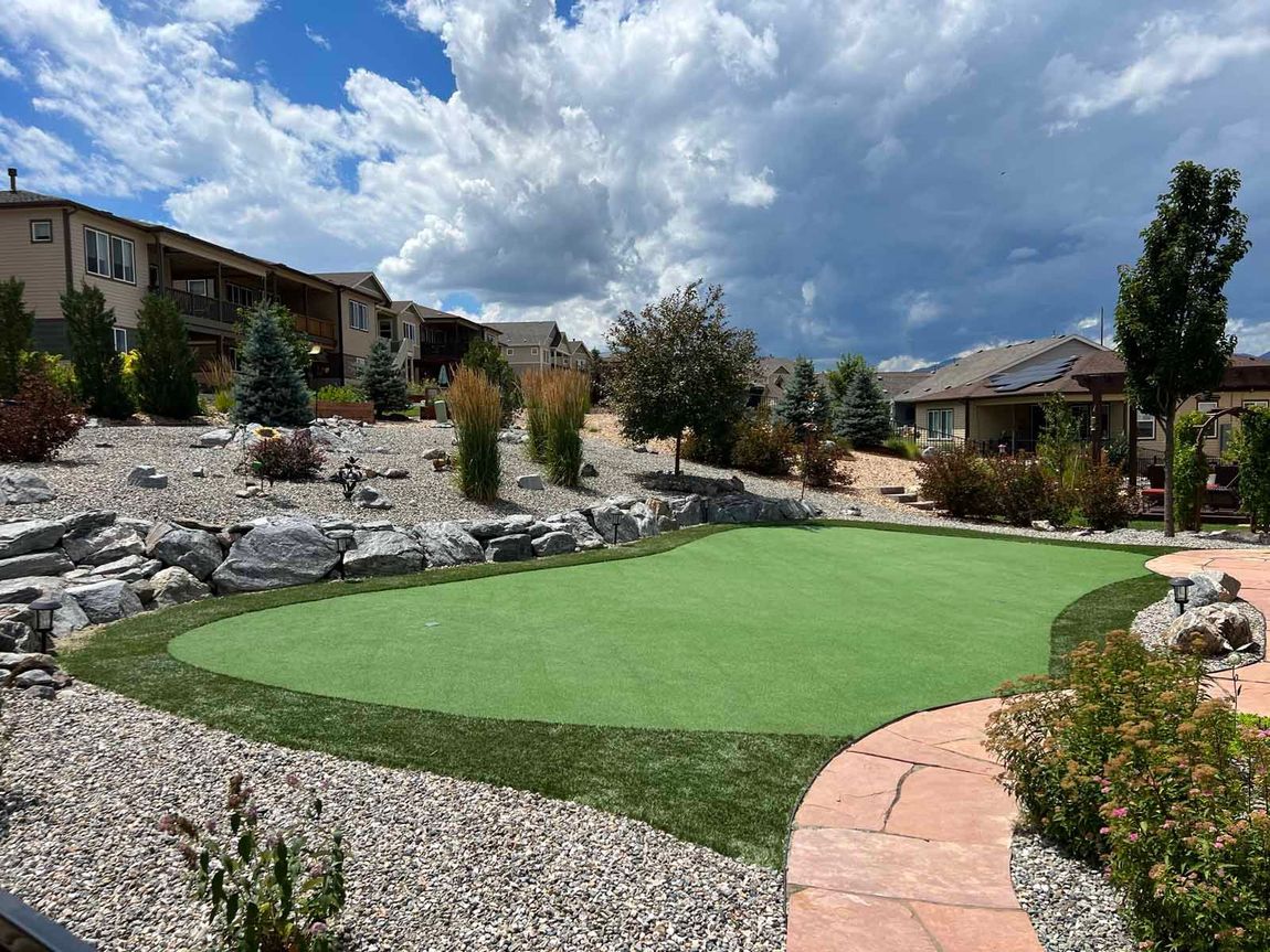 A green putting green in a backyard with houses in the background.