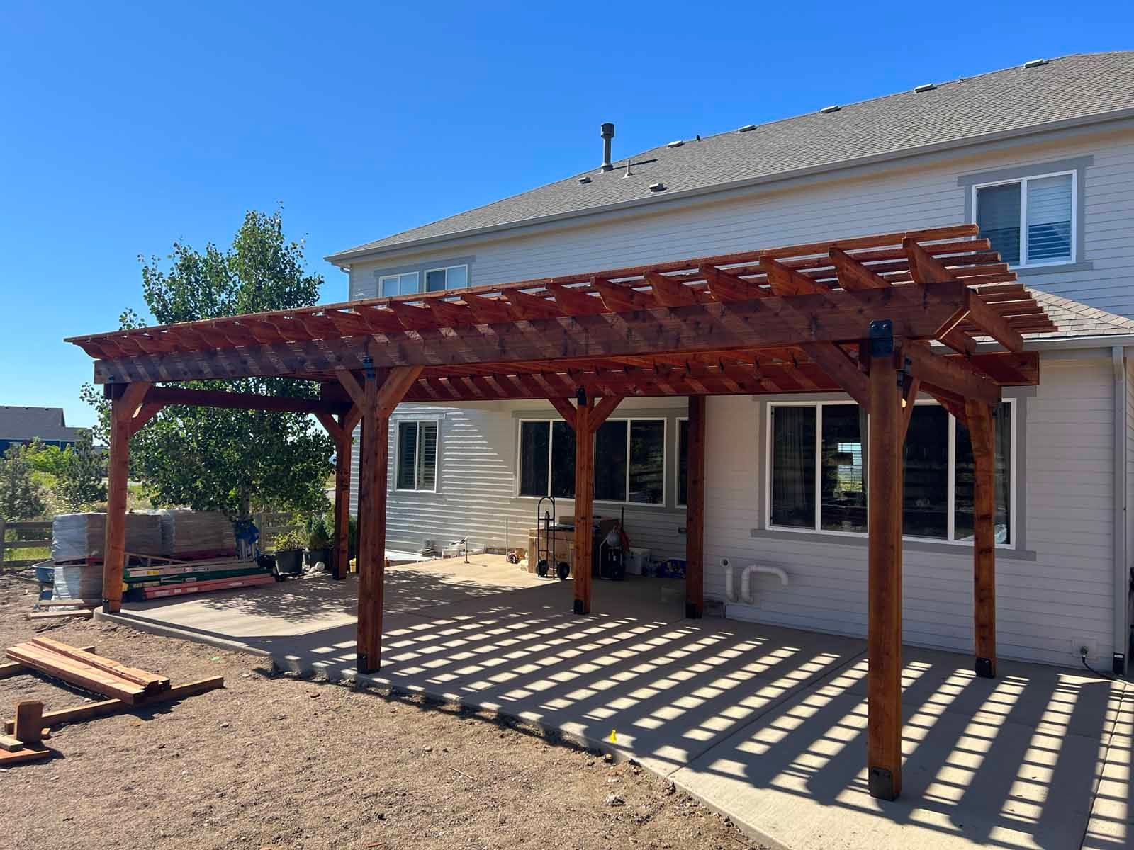 A wooden pergola is sitting in front of a house.